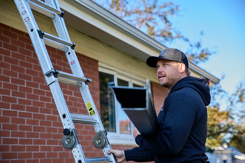 Installer carrying a new seamless gutter up a ladder